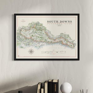 May include: A framed map of the South Downs National Park in England. The map is in a black frame and shows the park's topography, trails, and points of interest. The map is a detailed and informative guide to the park.