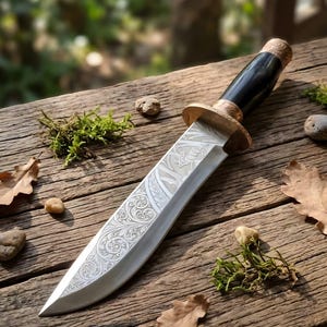 May include: A fixed-blade knife featuring a silver-toned steel blade with intricate floral and leaf engravings. The handle is made of a smooth, dark material with a metallic bolster and pommel, both decorated with detailed, embossed patterns.