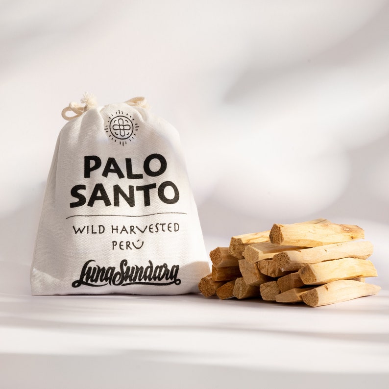 以下が含まれることがあります： 「PALO SANTO」の黒い文字と「WILD HARVESTED PERU」とLuna Sundaraのロゴがプリントされた白いキャンバスバッグ。バッグの隣には、薄茶色のパロサントの棒が積み重ねられています。