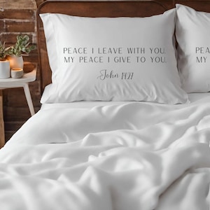 May include: White pillowcases with black text that reads "PEACE I LEAVE WITH YOU. MY PEACE I GIVE TO YOU. John 14:27" on one pillowcase and "PEA MY" on the other pillowcase.