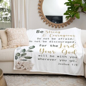 May include: White throw blanket with a floral design and a gold inspirational quote: "Be Strong & Courageous. Do not be afraid; do not be discouraged, for the Lord Your God will be with you wherever you go. Joshua 1:9"
