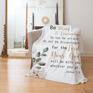May include: White fleece throw blanket with a floral design and gold lettering. The text reads "Be Strong & Courageous. Do not be afraid; do not be discouraged, for the Lord Your God will be with you wherever you go. Joshua 1:9"