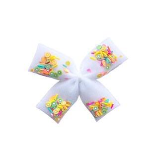 May include: A white tulle bow with colourful fruit-shaped sprinkles inside. The bow is tied in a knot and the sprinkles are visible through the tulle.