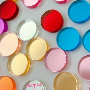 May include: A collection of colorful, round, acrylic embellishments in various shades including red, pink, yellow, blue, and gold. One piece has the text "30pcs Mixed Pack". These decorative pieces are ideal for craft projects.