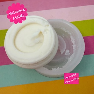 May include: A round, translucent silicone mould with a white circular insert inside. The image features pink text labels that read Silicone Mold! and Me Mold You Make. The mould has a smooth, flexible texture and a circular cavity for casting.