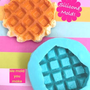 May include: A silicone waffle mould and a cooked waffle are shown against a colourful backdrop. The mould is blue, and the waffle is golden brown. Text on the image reads "Silicone Mold!" and "Me mold you make."