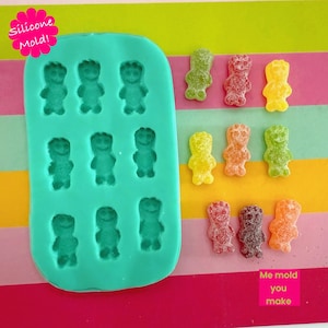 May include: A teal silicone mould with bear-shaped cavities, next to colourful gummy sweets. The sweets are in various colours, including green, red, yellow, and orange. The text "Silicone Mold!" and "Me mold you make" are visible.