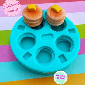 May include: A turquoise silicone mould with circular and square cavities, designed for crafting. Two stacks of miniature pancakes with yellow butter on top are displayed. The text "Silicone Mold!" and "ME MOLD YOU MAKE" are also visible.