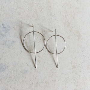Puede incluir: Un par de pendientes de plata con un diseño de círculo y línea recta.
