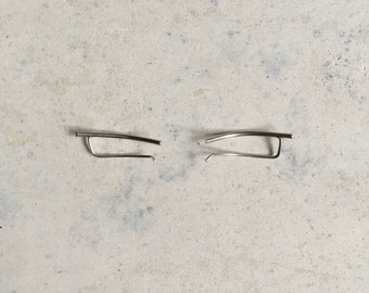 May include: A pair of silver-toned ear climber earrings featuring a smooth, curved bar design. Each earring consists of a single, slightly arched metal rod that extends along the earlobe, held in place by a thin, parallel wire backing.