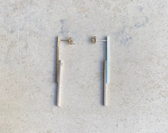 May include: A pair of silver-toned drop earrings featuring a vertical bar design. Each earring consists of a thin, straight metal post attached to a slightly longer, parallel rectangular bar that hangs freely, secured by a standard butterfly earring back.