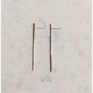 Peut inclure: Une paire de boucles d'oreilles en forme de barre dorée. Les boucles d'oreilles sont simples et minimalistes, avec un design de barre droite.