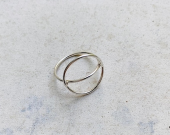 May include: A silver-colored ring featuring a thin, circular band design. The ring is constructed from a single continuous wire that forms a larger outer circle and a smaller inner circle, creating a layered, open-frame appearance with a polished finish.