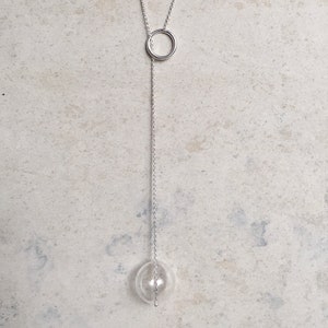 Peut inclure: Un collier en chaîne argent avec un pendentif circulaire et un orbe en verre transparent à l'extrémité.