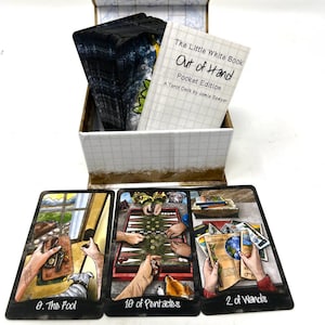 May include: A tarot deck set featuring a white box with a lid, containing a deck of cards and a small book titled "The Little White Book Out of Hand Pocket Edition". Three tarot cards are displayed: "0. The Fool", "10 of Pentacles", and "2 of Wands".