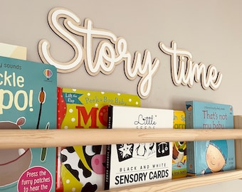 May include: A wooden shelf with a sign that says "Story time" above it. The shelf is filled with children's books, including "Peek-a-Boo Baby", "Little Seeds", "That's not my babu", and "Black and White Sensory Cards".