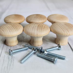 May include: Six wooden mushroom-shaped cabinet knobs with a natural wood finish and silver screws.