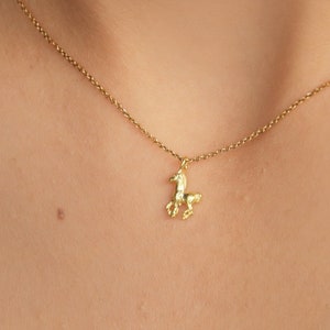 May include: A delicate gold-colored necklace featuring a small, textured horse pendant. The horse charm is suspended from a fine chain, creating a minimalist and elegant look. The necklace is shown against a dark background.