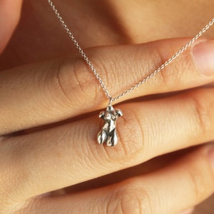 Peut inclure: Un collier en cha&icirc;ne argent avec un petit pendentif en argent abstrait. Le pendentif a la forme d'une personne avec les bras lev&eacute;s.