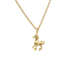 May include: A gold-colored necklace with a small horse pendant. The horse is in a running pose, and the chain is delicate. The necklace is set against a white background.
