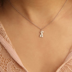 Peut inclure: Un collier en argent avec un pendentif d&eacute;licat en forme de silhouette humaine. Le collier est port&eacute; par une personne &agrave; la peau l&eacute;g&egrave;rement brune. La personne porte un haut en dentelle rose clair.