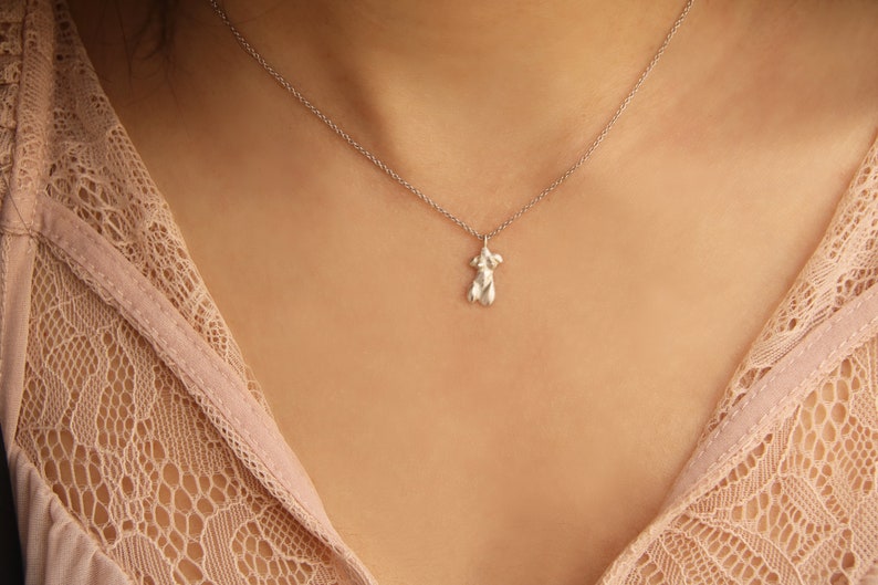 Peut inclure: Un collier en argent avec un pendentif d&eacute;licat en forme de silhouette humaine. Le collier est port&eacute; par une personne &agrave; la peau l&eacute;g&egrave;rement brune. La personne porte un haut en dentelle rose clair.