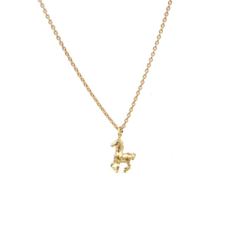 May include: A gold-colored necklace with a small horse pendant. The horse is in a running pose, and the chain is delicate. The necklace is set against a white background.