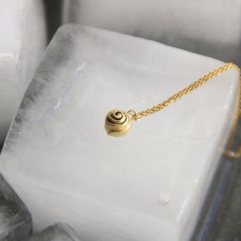 Op de afbeelding: Een goudkleurige hangerketting met een kleine, spiraalvormige bedel. De bedel hangt aan een fijne gouden ketting. De ketting wordt gepresenteerd tegen een witte achtergrond.
