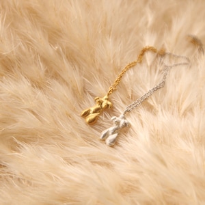 Peut inclure: Deux colliers d&eacute;licats avec un pendentif en forme de figurine abstraite unique. L'un est en or et l'autre en argent. Les colliers sont pr&eacute;sent&eacute;s sur un fond doux et moelleux de couleur beige.