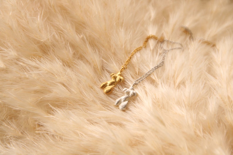 Peut inclure: Deux colliers d&eacute;licats avec un pendentif en forme de figurine abstraite unique. L'un est en or et l'autre en argent. Les colliers sont pr&eacute;sent&eacute;s sur un fond doux et moelleux de couleur beige.