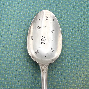 Peut inclure: Une cuillère en argent avec un thème de Noël. La cuillère est décorée d'hommes en pain d'épices.
