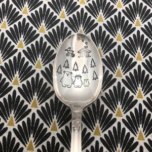 Peut inclure: Une cuillère en argent gravée d'un motif représentant une famille d'ours dans un décor de forêt. Le motif comprend une petite maison, une poussette et plusieurs sapins. La cuillère est un cadeau unique et personnalisé pour une nouvelle famille.