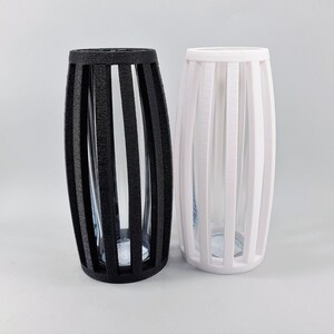 May include: Two decorative vases, one black and one white, with a vertical slat design. Each vase has a clear glass insert. The vases are cylindrical with an oval shape.