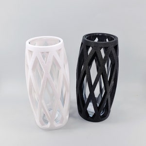 May include: Two decorative vases. One is white, the other is black. Both have a lattice design around a clear glass interior. The vases are cylindrical with an oval shape.