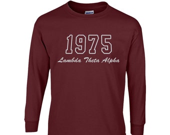 Puede incluir: Una camiseta de manga larga color burdeos con el año "1975" en letras blancas y las palabras "Lambda Theta Alpha" en cursiva. La camiseta es de material suave y tiene cuello redondo.