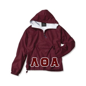 May include: A maroon hooded anorak jacket with a white interior lining. The jacket features a front pocket, a half-zip closure, and a drawstring at the hem. The letters "ΛΘA" are printed in white on the front.