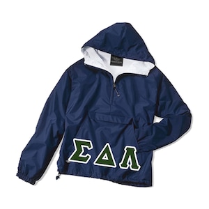 May include: Navy blue hooded anorak jacket with a white interior lining. The jacket features a half-zip closure, a front pocket, and a drawstring at the hem. The Greek letters ΣΔΛ are displayed in green and white on the front of the jacket.