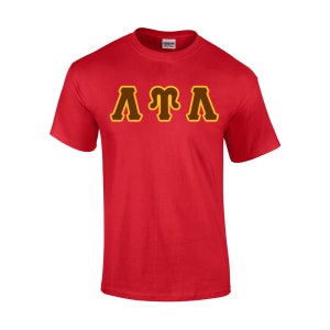 May include: A red t-shirt with the letters "ATA" in a brown and yellow design across the chest. The shirt is made of a soft material and has short sleeves. The Gildan logo is visible on the collar.