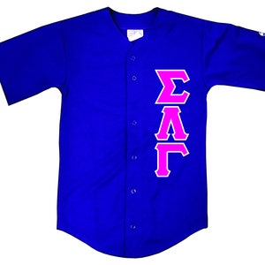 May include: A royal blue baseball jersey with a pink "ΣΑΓ" Greek letter design on the right side.