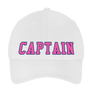 May include: A white baseball cap with the word "CAPTAIN" in pink block letters outlined in navy blue. The hat has a curved brim and a rounded crown, suitable for sun protection.
