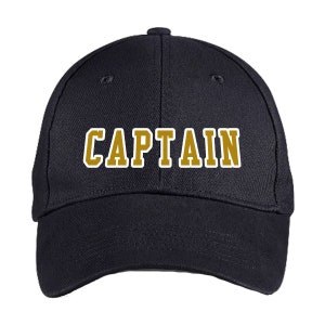 May include: A navy blue baseball cap with the word "CAPTAIN" in gold block letters with a white outline. The cap has a curved brim and a button on top.