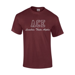 May include: A maroon t-shirt with the word "ACE" in white block letters and the words "Lambda Theta Alpha" in cursive script. The shirt is made of a soft material and has short sleeves.