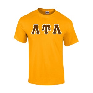 May include: Mustard yellow t-shirt with the letters ATA in a brown and white collegiate font. The short-sleeved shirt is made of a soft material and is suitable for casual wear.