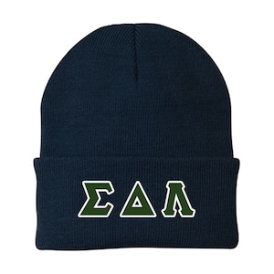 May include: A navy blue knit beanie with the Greek letters ΣΔΛ in dark green with a white outline. The beanie is a classic style, suitable for cold weather.