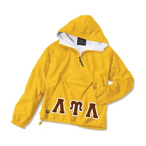 May include: A yellow hooded anorak jacket with a white interior lining. The jacket features a half-zip closure, a front pocket, and the Greek letters "ΛΤΛ" in brown. The jacket is designed for outdoor wear.