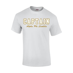 May include: White t-shirt with the word "CAPTAIN" in gold block letters, with "Alpha Phi Lambda" below. The shirt is a crew neck style and appears to be made of cotton. The Gildan brand label is visible on the collar.
