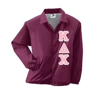 May include: Burgundy colored jacket with a snap closure and a vertical pink KAX design on the right side.