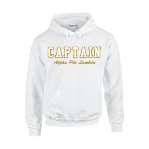 May include: White hooded sweatshirt with the word "CAPTAIN" in gold block letters above "Alpha Phi Lambda". The sweatshirt has a front pocket and a drawstring hood. The Gildan logo is visible on the hood.
