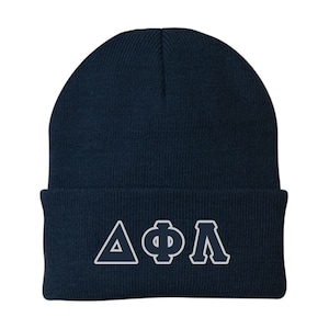 May include: A navy blue knit beanie with white Greek letters. The beanie is a classic style, with a folded cuff and a ribbed texture. The letters are outlined in white and are centered on the front of the hat.