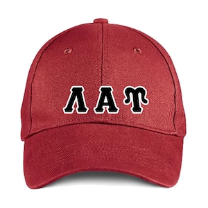 May include: A maroon baseball cap with the letters "AAT" in white with a black outline. The cap has a curved brim and a button on top. The letters are in a bold, blocky font.